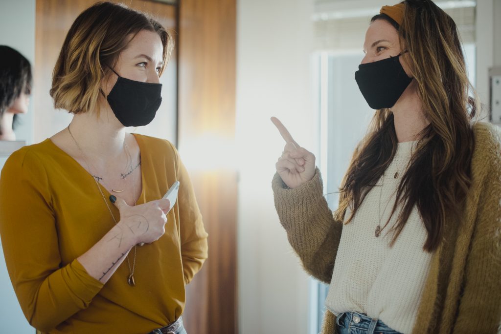 Refinery House owner Heidi Epp points at co-owner Aly McRae while they both smile behind masks